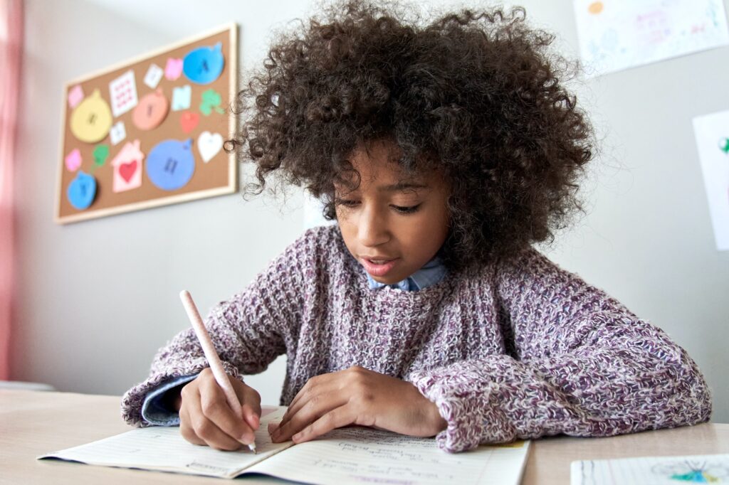 Happy african school child girl studying writing homework, learning at home.