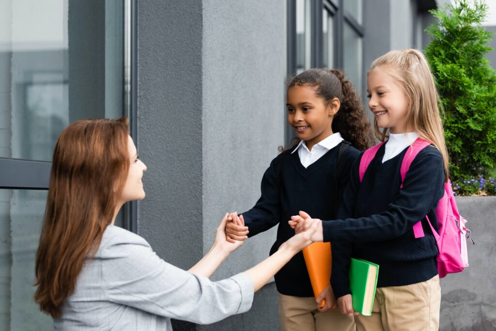 happy mother holding hands of daughters smiling and holding books