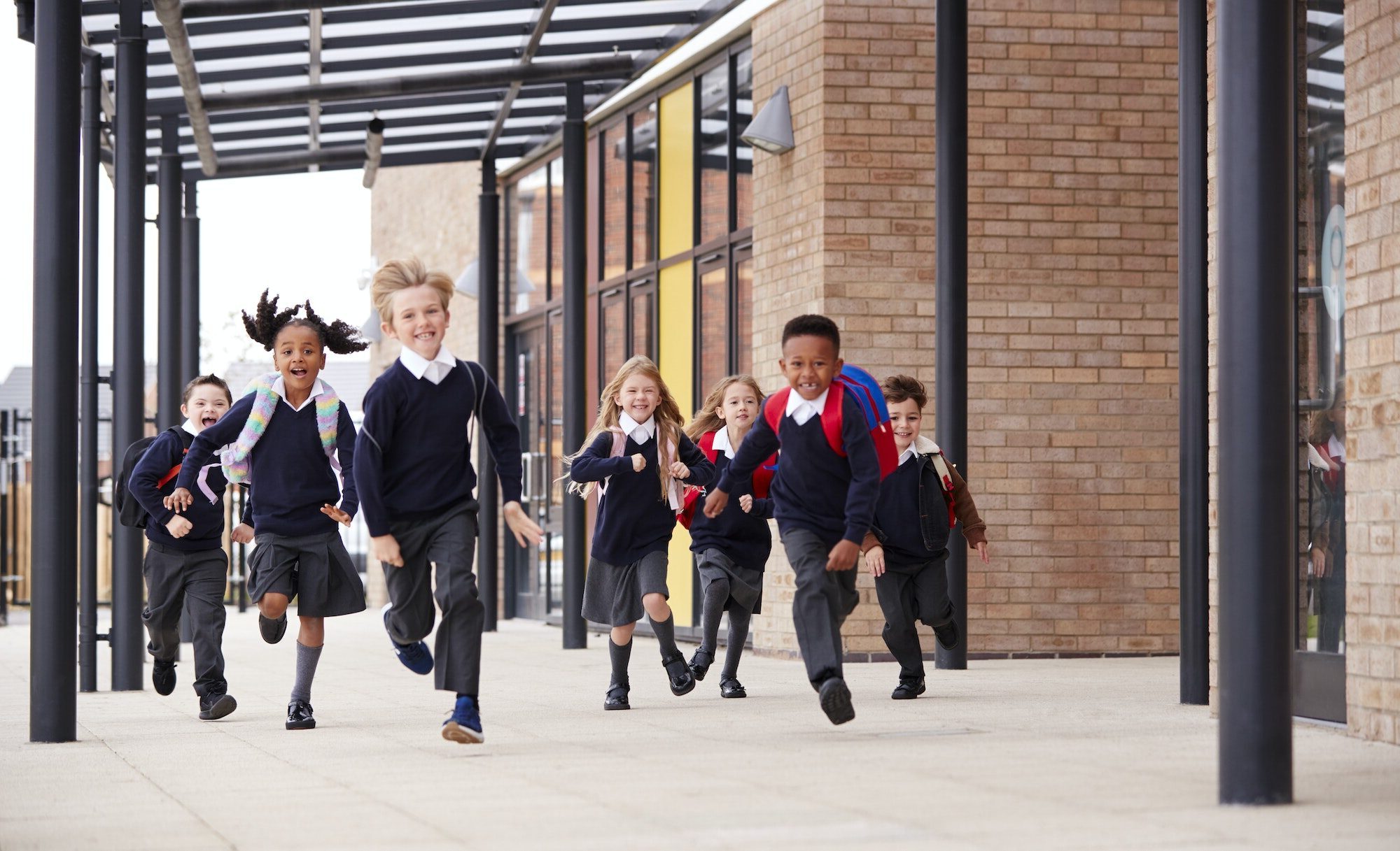 Primary school kids, wearing school uniforms and backpacks, running on a walkway